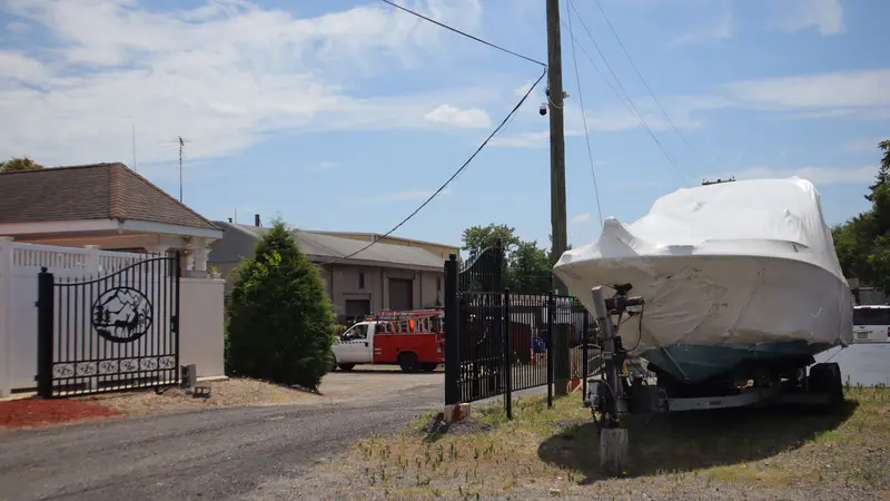 A covered boat on its trailer in the yard by the gate