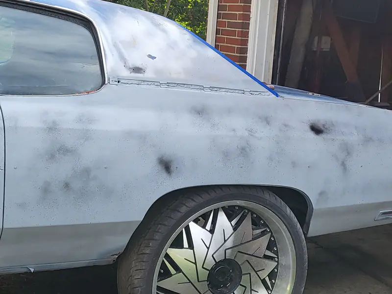 A classic coupe in primer with its trim taped off for paint