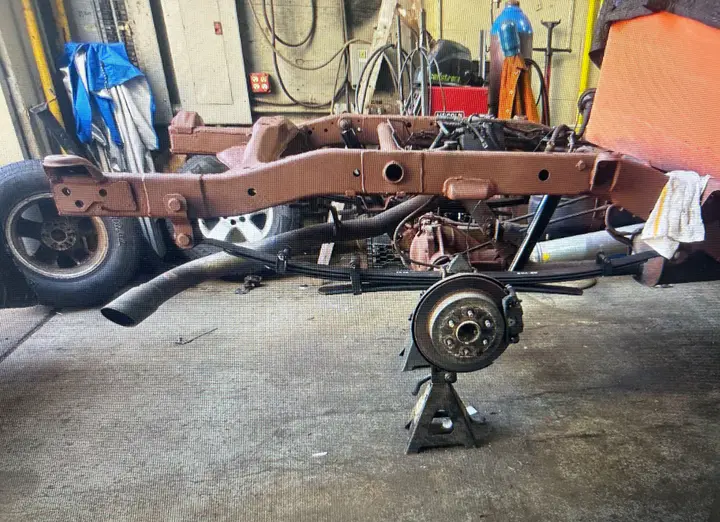 The repaired frame in red primer on stands, with the rear brake assembly beside it