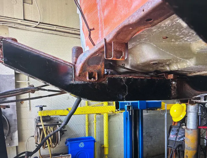 A new black steel rail section welded into a rusty truck frame, the truck up on the lift