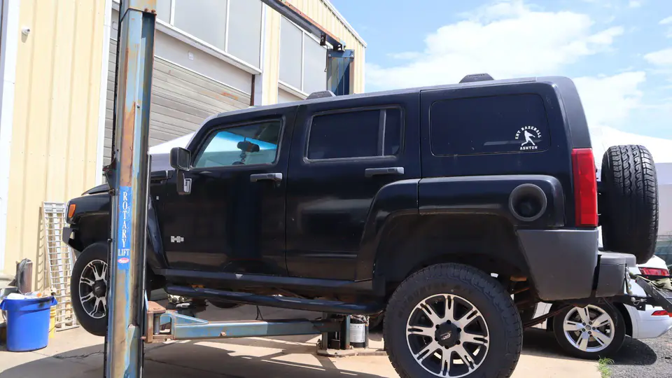 A black Hummer up on a two-post lift outside the shop bays