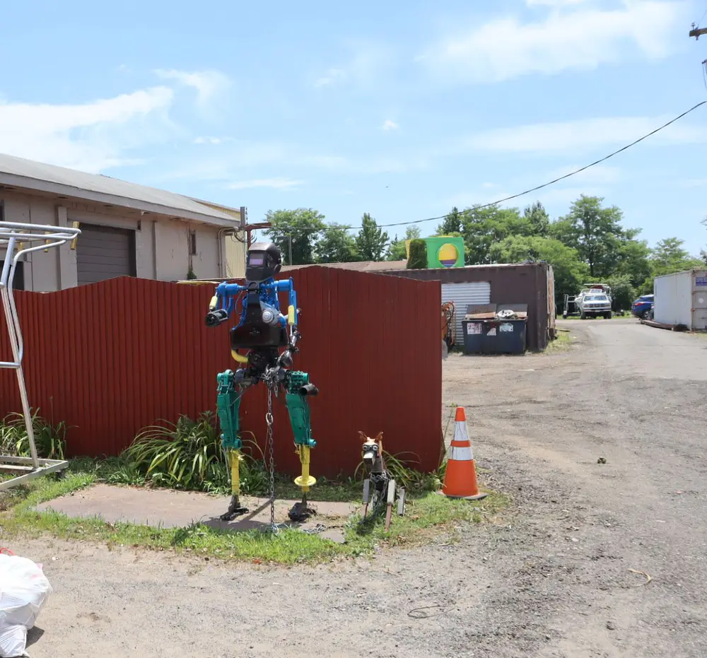 A scrap-metal robot sculpture standing by the shop fence