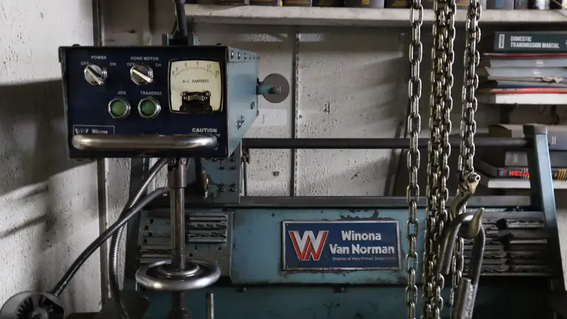 A Winona Van Norman machine with its control panel and a hoist chain beside it
